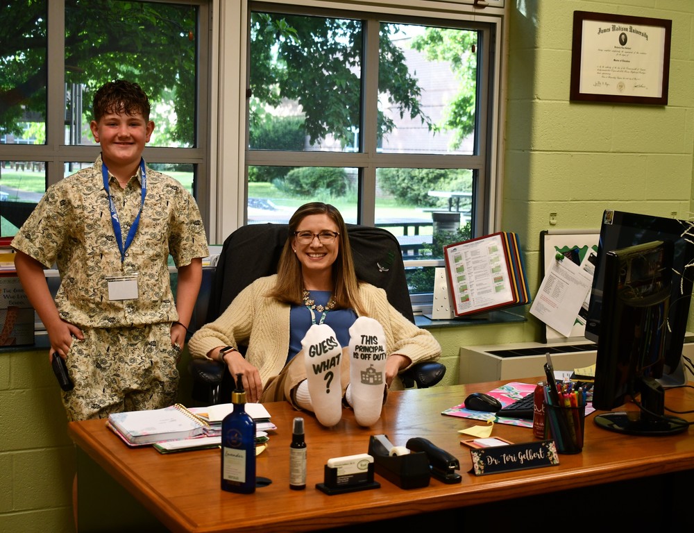 principal with feet on the desk wearing socks that says she is off duty with student next to her