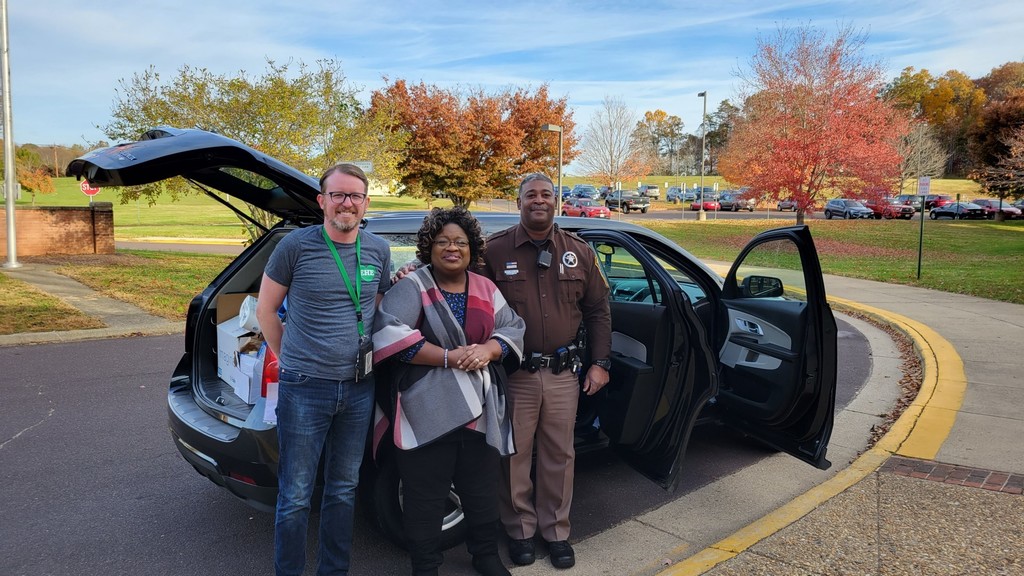 Mr. Foster, Mrs. White, and Deputy White in front of a car full of donations