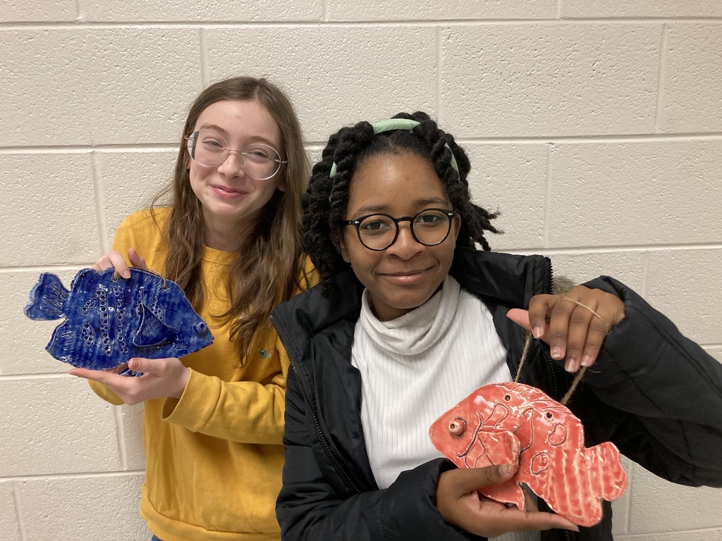 A picture of two students holding up their clay fish creations
