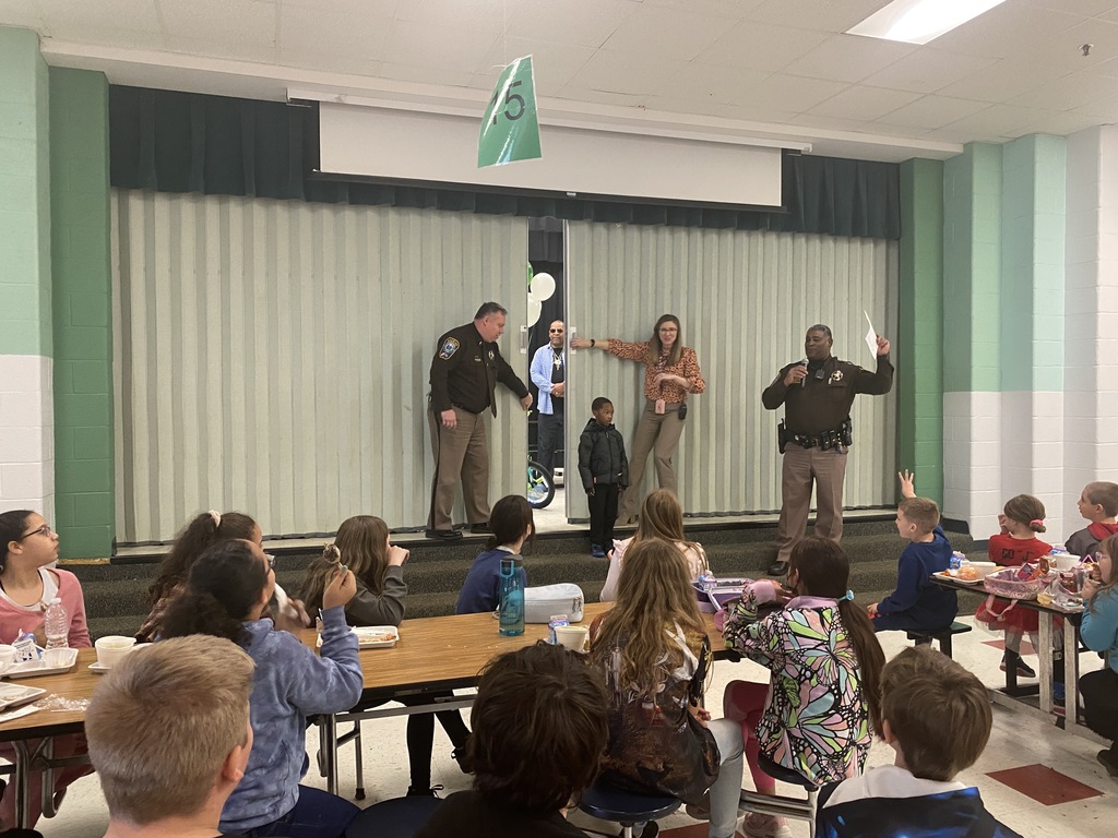 sheriff's deputy and principal open curtain on stage with young student