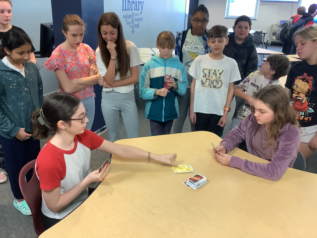 a picture of two students playing uno with a crowd of students watching.