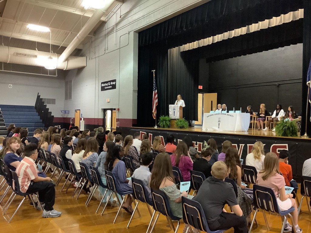 a picture of the new NJHS members  sitting, and Mrs. Sprunger speaking from the stage and podium. 
