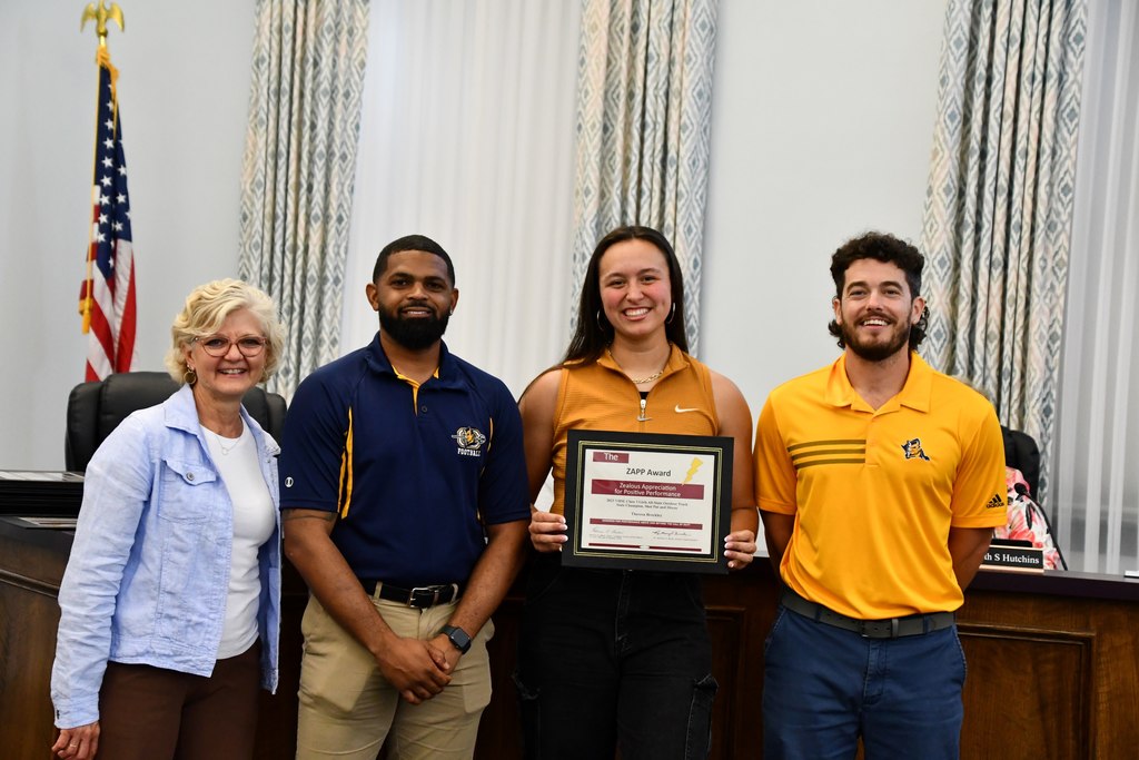 student holding award with coaches and board member 