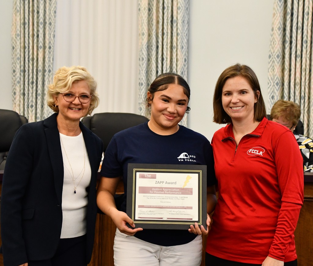 student holding award with board member and teacher