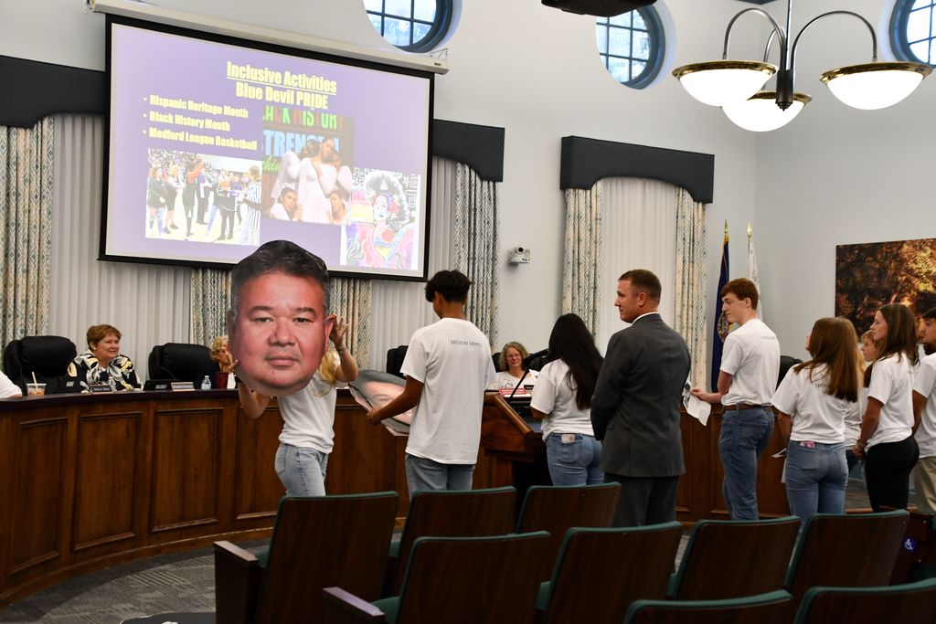 student holding fathead of teacher in board room
